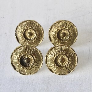 May include: Four antique brass cabinet knobs with a floral design. Each knob is round with a detailed, raised pattern of petals and a central, recessed circle. The knobs are a warm, golden color and are set against a white background.