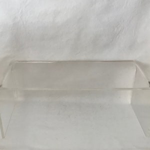May include: A clear acrylic bench with a simple, modern design. The bench is made of thick, durable acrylic and has a sleek, minimalist look.