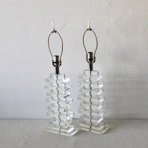 May include: A pair of clear acrylic lamps with a stacked block design. The lamps have a silver metal base and a clear glass shade.