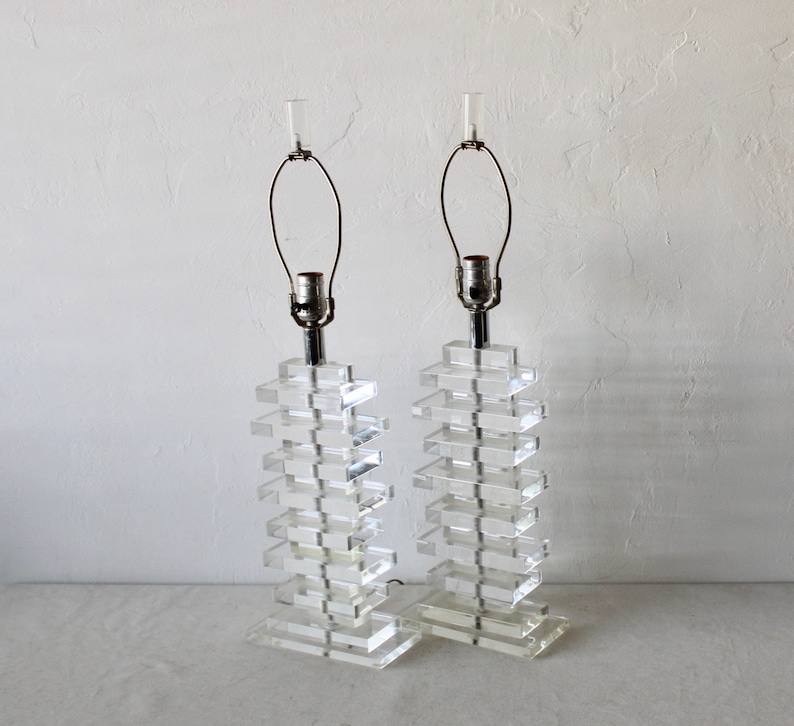 May include: A pair of clear acrylic lamps with a stacked block design. The lamps have a silver metal base and a clear glass shade.