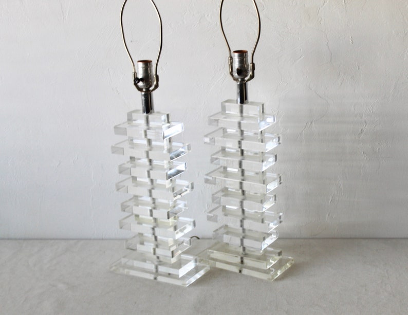 May include: A pair of clear acrylic table lamps with a stacked design. Each lamp has a silver metal base and a clear glass shade.