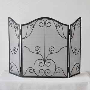 Puede incluir: Pantalla de chimenea de metal negro con un diseño de tres paneles. La pantalla presenta un diseño ornamental y enrollado en cada panel. La pantalla de malla está enmarcada por un borde decorativo. La pantalla está diseñada para sostenerse por sí sola.
