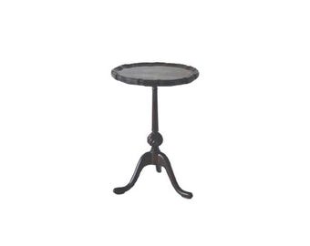 Pode incluir: Uma mesa lateral em estilo antigo, castanho escuro, com um tampo redondo e uma borda decorativa ondulada. A mesa tem um único suporte central com um nó decorativo e três pernas curvas. A mesa tem aproximadamente 61 cm de altura.