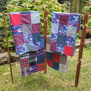 May include: Two patchwork quilts with a Buffalo Bills theme. The quilts are made of denim, plaid, and red fabric with the Buffalo Bills logo and the word "Bills" repeated throughout. The quilts are hanging on a wooden rack.