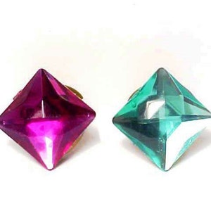May include: Two square-shaped, faceted, decorative gems. One is a bright pink and the other is a bright teal green.