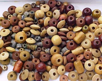 May include: A collection of wooden beads in various shapes and sizes, including round, disc, and cylindrical. The beads are in shades of brown, tan, and cream, with visible holes for stringing. A variety of natural tones and textures are visible.