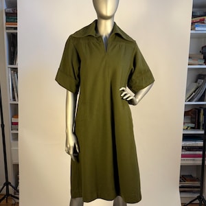 May include: Olive green dress with short sleeves and a collared neckline. The dress has a relaxed fit and falls to the mid-calf. The sleeves have a folded cuff detail. The dress is displayed on a mannequin.