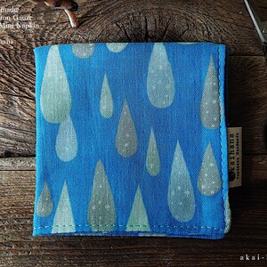 May include: A square blue cotton gauze handkerchief featuring a repeating pattern of light green and white raindrops. The fabric has a visible woven texture and a small side tag labeled akaihana. The text reads Japanese Handmade Quadruple-Cotton Gauze Handkerchief Mini Napkin by akaihana.