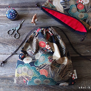 May include: Japanese handmade drawstring purse with a black background and a floral pattern in gold, red, and green. The purse is made of fabric and has a drawstring closure. The purse is sitting on a wooden surface.