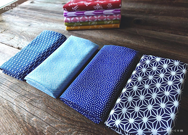 Puede incluir: Cuadrados de tela plegados con varios patrones y colores se muestran sobre una superficie de madera. Una pila de telas estampadas adicionales est&aacute; en el fondo. Las telas presentan dise&ntilde;os azules, celeste, rojos, morados, rosas y amarillos.