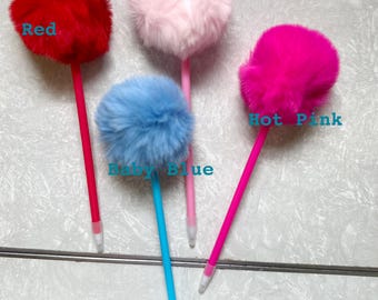 Op de afbeelding: Vier pluche pompon pennen in rood, baby roze, fel roze en babyblauw. De pennen hebben witte dopjes en liggen op een betegelde ondergrond.