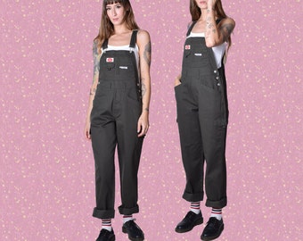 May include: A pair of dark green overalls with a red logo on the front. The overalls have a relaxed fit and are cuffed at the ankles.