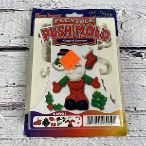 Puede incluir: Un molde flexible para manualidades, con un Papá Noel, un muñeco de nieve, un árbol de Navidad y otras formas temáticas navideñas. El paquete es blanco, azul y naranja, con el texto "FLEXIBLE PUSH MOLD" y "Kringle & Snowman".