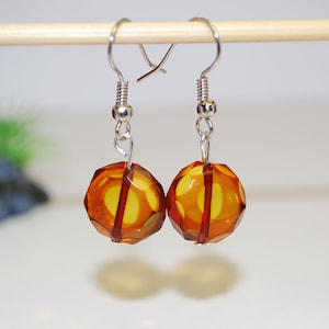 May include: A pair of amber earrings with silver hooks. The amber is faceted and has a warm, honey-like colour.