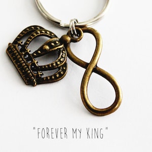 May include: A gold-toned keychain with a crown charm and an infinity symbol charm. The keychain has a silver key ring. The text "FOREVER MY KING" is printed below the charms.