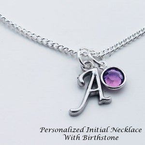 May include: A silver chain necklace with a silver charm featuring the letter "A" and a purple birthstone. "Personalized Initial Necklace With Birthstone" is written below the charm.