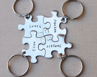 May include: Four silver puzzle piece keychains connected together. Each piece is engraved with a name and a heart. The keychains are attached to silver keyrings. The names on the keychains are Capri, Eden, Ashlan, and Shaylee.