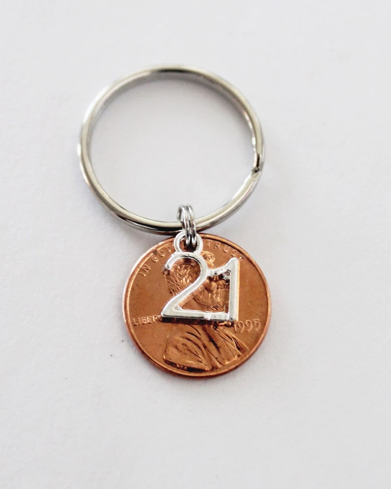 May include: A silver key chain with a 1995 penny attached. The penny has a silver charm with the number 21 on it.