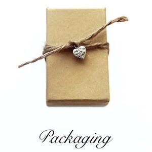 Pu&ograve; includere: Una piccola scatola di cartone marrone legata con uno spago e un ciondolo a forma di cuore argentato che dice "Made with Love".