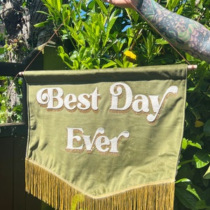 May include: Green velvet banner with gold fringe and white lettering that reads "Best Day Ever".