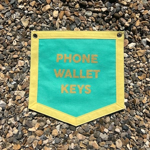 May include: A turquoise blue canvas banner with yellow trim and the words "PHONE WALLET KEYS" in gold glitter lettering.