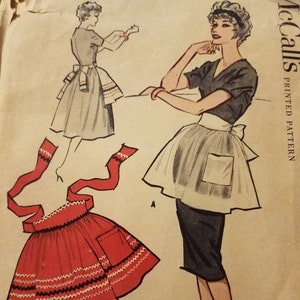 May include: A vintage sewing pattern for a red and white apron with a pocket. The pattern includes instructions for two different styles of aprons, one with a full skirt and one with a shorter skirt. The pattern is from McCall's and is printed on a light brown paper.