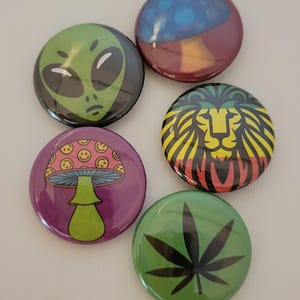 May include: Set of five round buttons with various designs. Includes a green alien face, a blue and maroon abstract design, a mushroom with smiley faces, a lion with yellow, green, and red stripes, and a green cannabis leaf.
