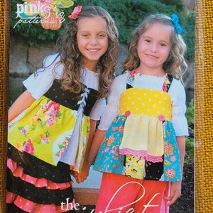 May include: Two girls wearing colorful dresses and a floral print top. The girl on the left is wearing a black and white polka dot skirt with a ruffle trim. The girl on the right is wearing a yellow and white polka dot top with a ruffle trim. The text "the juliet top No. 17" is printed on the bottom of the image.