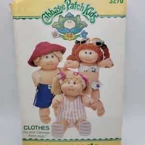 May include: A Butterick sewing pattern envelope for Cabbage Patch Kids clothes, number 3270. The front features three dolls wearing various outfits including a red hat, blue shorts, a white bikini, and a white striped romper with pink hair bows.