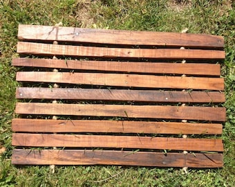May include: A wooden slatted mat with natural rope ties. The mat is made of dark brown wood and has a rustic look.