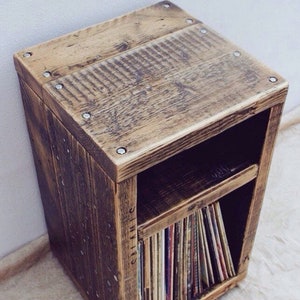 May include: A rustic wooden record shelf with a single shelf and a top surface. The shelf is made of reclaimed wood and has a dark brown finish. The shelf is filled with vinyl records.