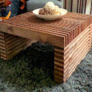 May include: A square wooden coffee table with a unique slatted design. The table is made of natural wood with a rich brown color. The table is sitting on a rug.