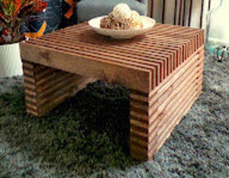 May include: A square wooden coffee table with a unique slatted design. The table is made of natural wood with a rich brown color. The table is sitting on a rug.