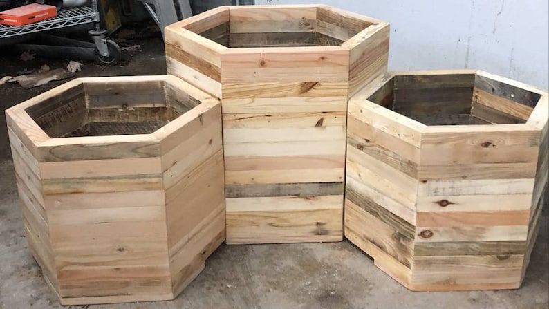 May include: Three hexagonal wooden planters made from reclaimed wood. The planters are different sizes and are arranged in a staggered formation.