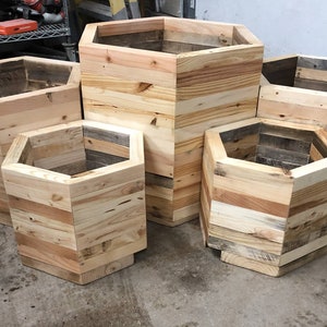 May include: Five hexagonal wooden planters made from reclaimed wood. The planters are different sizes and are arranged in a staggered pattern.