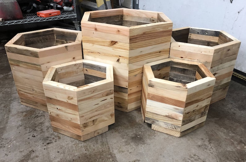 May include: Five hexagonal wooden planters made from reclaimed wood. The planters are different sizes and are arranged in a staggered pattern.