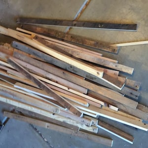 May include: A pile of reclaimed wood scraps in various shades of brown, beige, and white. The wood is in various lengths and widths, and some pieces have knots or other imperfections.