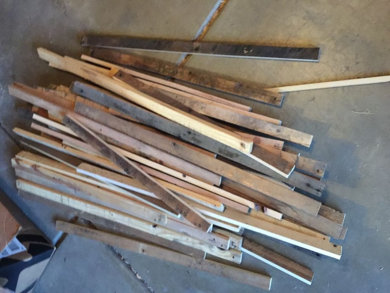 May include: A pile of reclaimed wood scraps in various shades of brown, beige, and white. The wood is in various lengths and widths, and some pieces have knots or other imperfections.