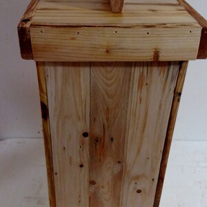 May include: A wooden box with a simple design, made from reclaimed wood planks. The box has a hinged lid with a small wooden handle on top. The box is a light brown color and has a natural wood finish.
