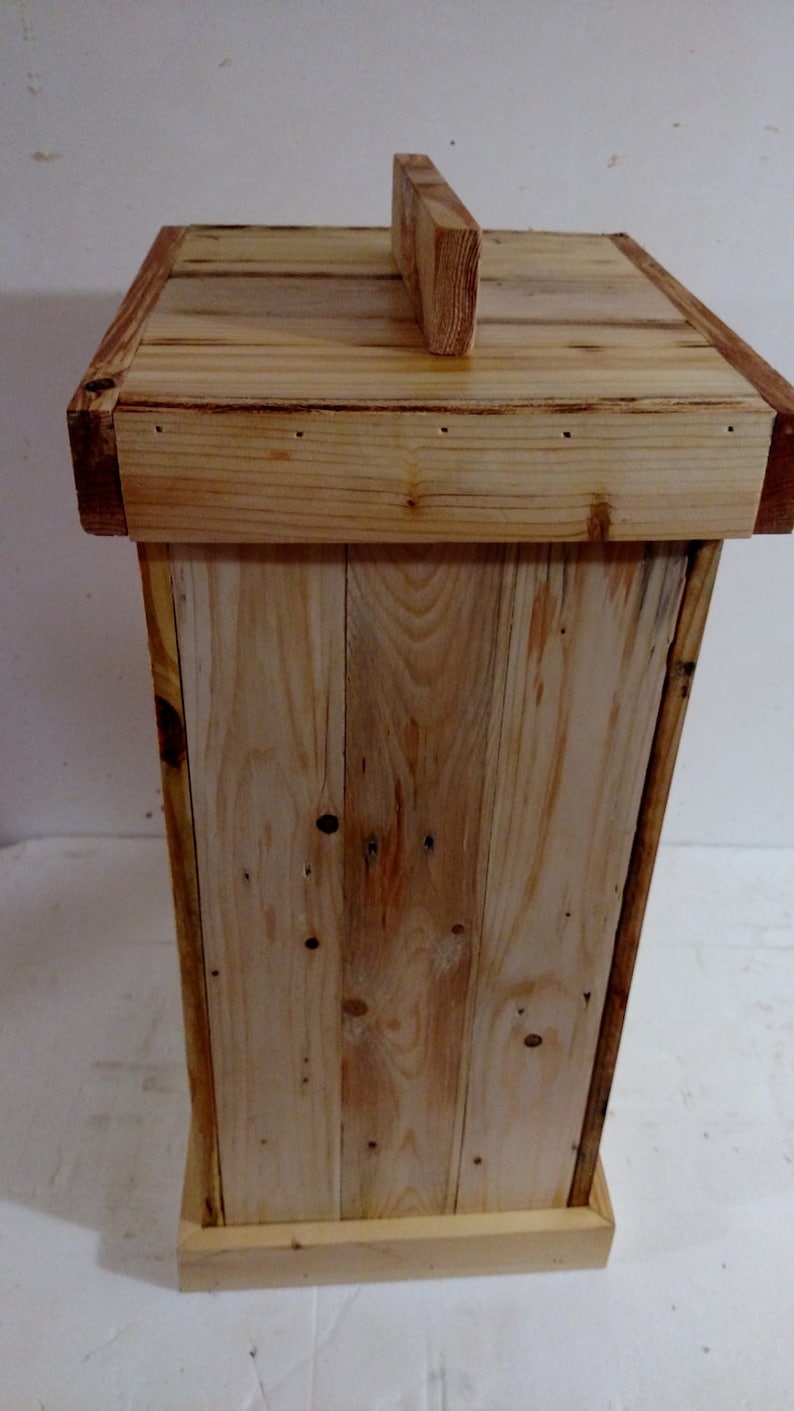 May include: A wooden box with a simple design, made from reclaimed wood planks. The box has a hinged lid with a small wooden handle on top. The box is a light brown color and has a natural wood finish.