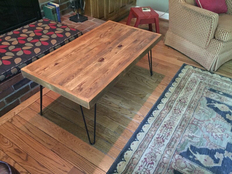 May include: A rectangular wooden coffee table with a natural finish. The table has a thick, solid wood top and is supported by four black hairpin legs. The table is approximately 48 inches long and 24 inches wide.