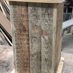 May include: A rustic wooden trash can with a natural wood finish. The can is made of reclaimed wood planks and has a simple, rectangular shape.