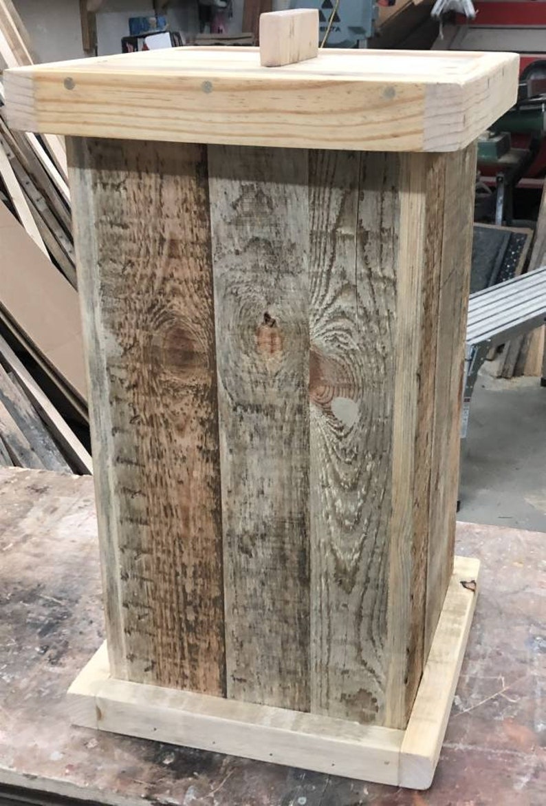May include: A rustic wooden trash can with a natural wood finish. The can is made of reclaimed wood planks and has a simple, rectangular shape.