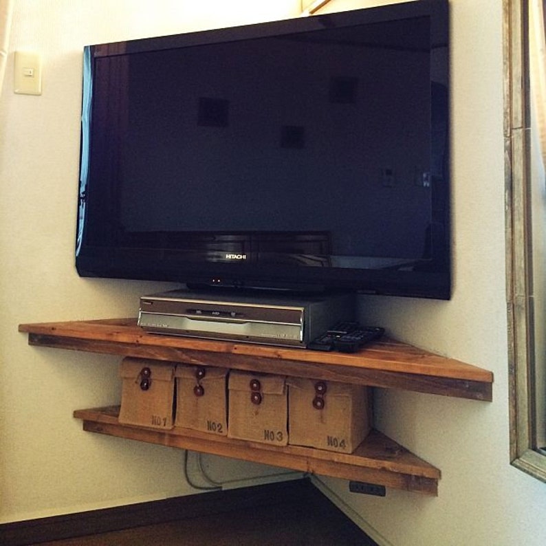 Puede incluir: Un televisor de pantalla plana Hitachi negro montado en una estanter&iacute;a de esquina de madera. Debajo del televisor hay un reproductor de DVD y un mando a distancia. La estanter&iacute;a tiene tres niveles, con cuatro cajas de almacenamiento numeradas en la parte inferior. La estanter&iacute;a es de madera marr&oacute;n claro.