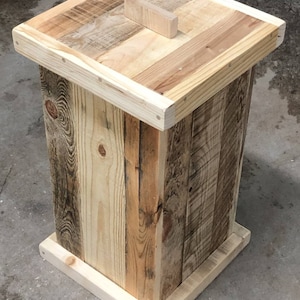 May include: A wooden trash can with a lid made from reclaimed wood. The can has a square base and a rectangular body. The lid has a small wooden handle.