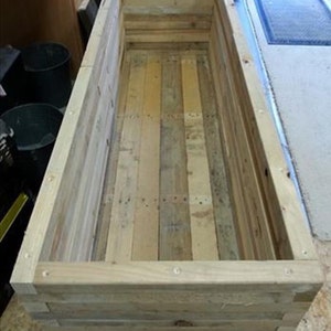 Op de afbeelding: Een houten plantenbak gemaakt van gerecycled pallet hout. De plantenbak is rechthoekig en heeft een natuurlijke hout afwerking.