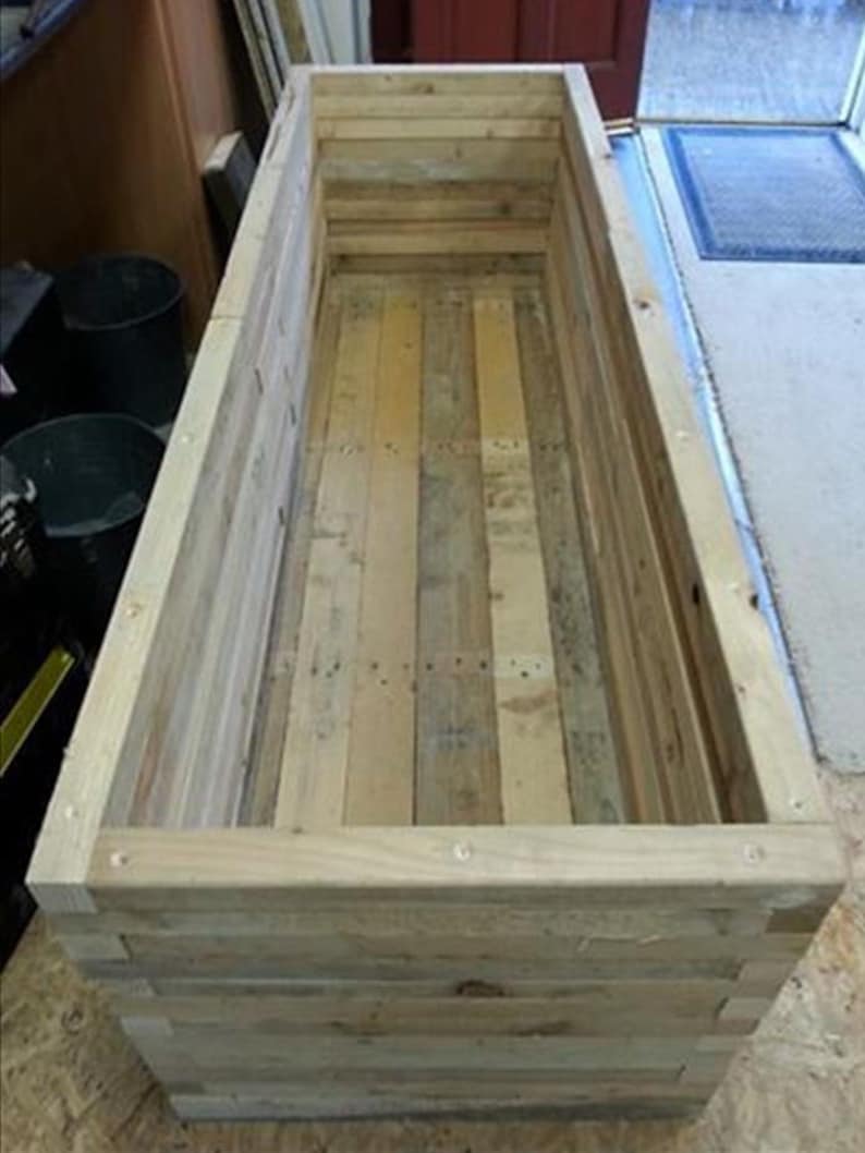 Op de afbeelding: Een houten plantenbak gemaakt van gerecycled pallet hout. De plantenbak is rechthoekig en heeft een natuurlijke hout afwerking.