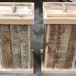 May include: Two wooden trash cans with lids. The cans are made of reclaimed wood and have a rustic look. The lids have a simple handle.