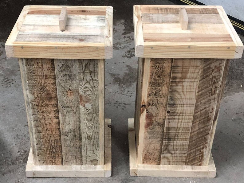 May include: Two wooden trash cans with lids. The cans are made of reclaimed wood and have a rustic look. The lids have a simple handle.