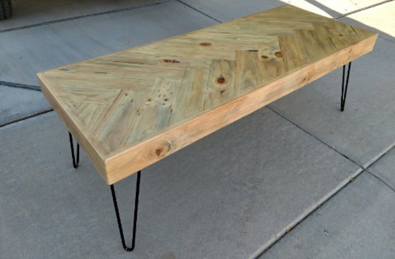 May include: A rectangular coffee table with a light wood herringbone pattern top. The table has a natural finish and is supported by four black hairpin legs. The table measures approximately 48 inches long.